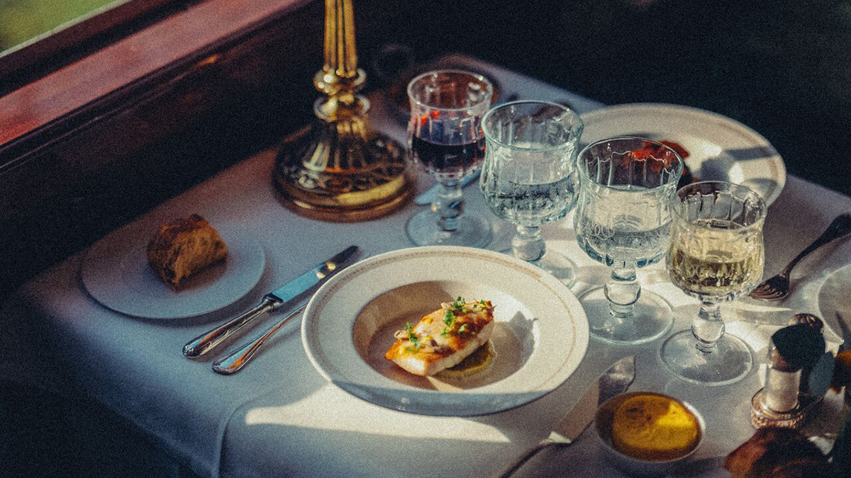 A plated meal and wine glasses set beside a train window aboard the Venice Simplon-Orient-Express