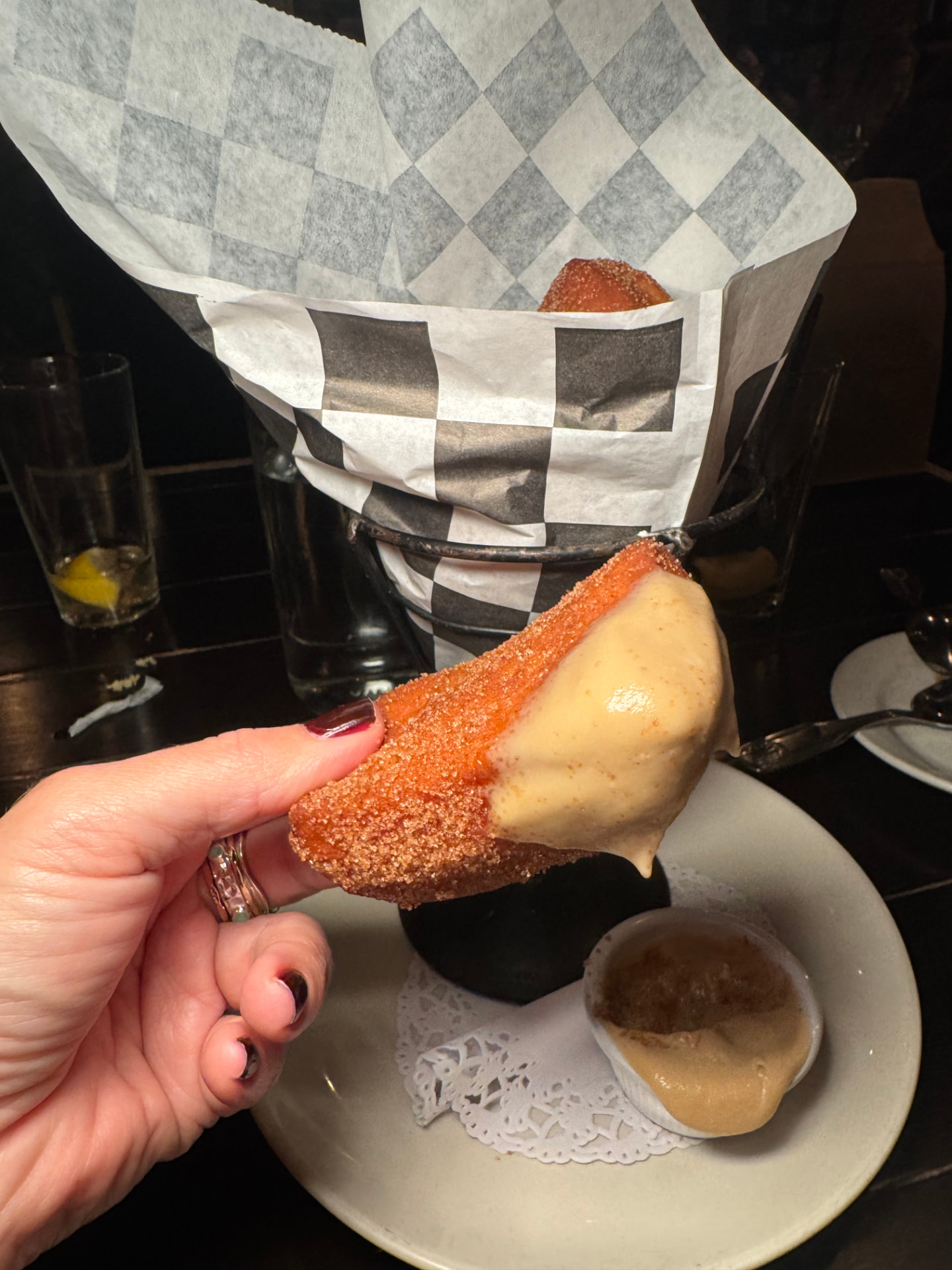 A beignet dipped in apple sauce, with a basket of beignets behind it